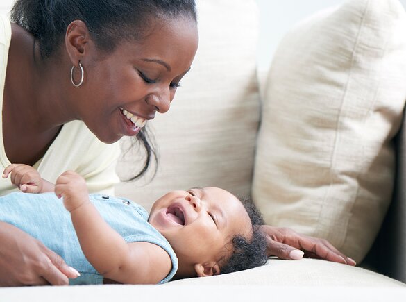 Uma mãe brinca com o seu bebé num sofá.