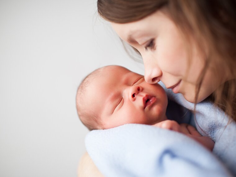 A mother holds her sleeping newborn close to her face.