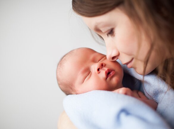 A mother holds her sleeping newborn close to her face.