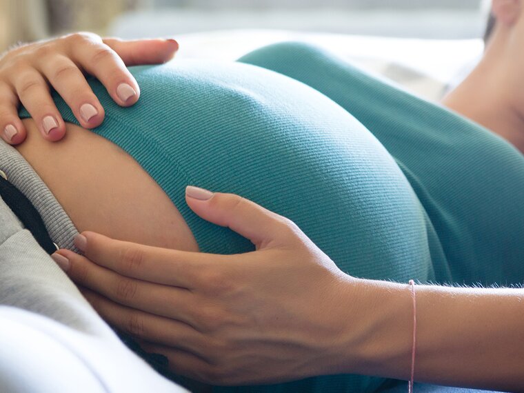 Una mujer está tumbada y se sujeta el vientre de embarazada.