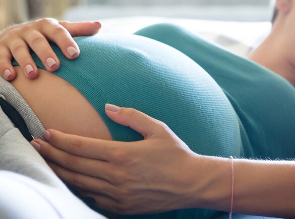 Uma mulher está deitada e segura a sua barriga de grávida.