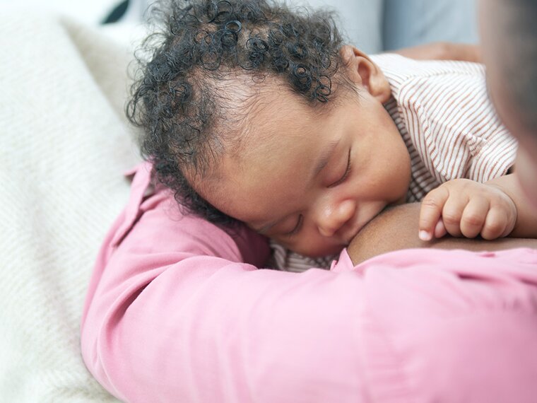 A baby breastfeeding on its mom's lap while at home.