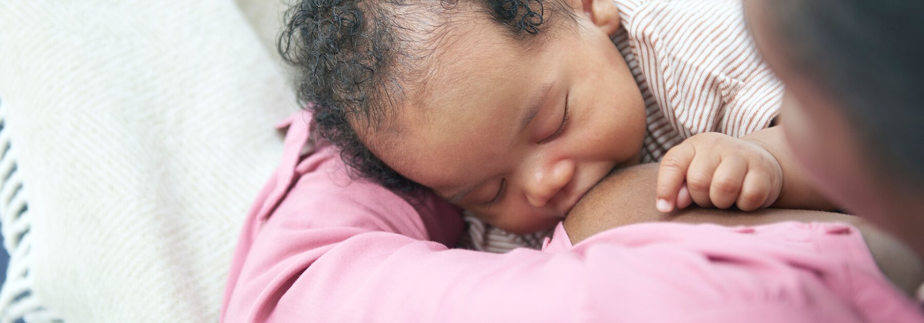 A baby breastfeeding on its mom's lap while at home.