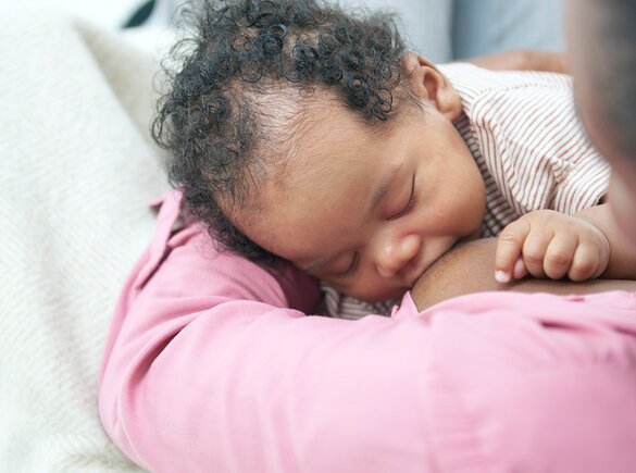 A baby breastfeeding on its mom's lap while at home.