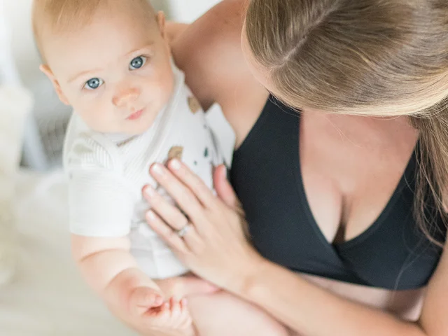 A baby looks into the camera above while being held by its mom.