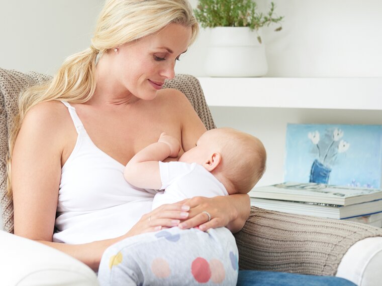 Een moeder zit thuis op de stoel en geeft haar baby borstvoeding.