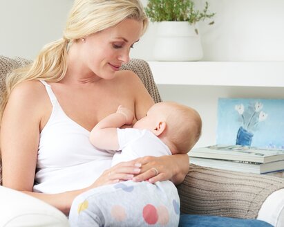 A mum is sitting on the chair at home breastfeeding her baby.