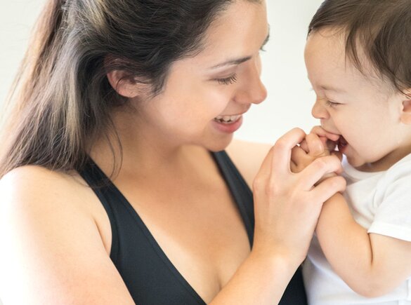 A baby tries to put his hands in his mouth and his mother playfully holds his hands, making them smile.