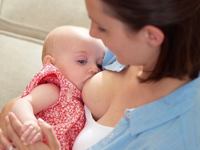 A mother is at home breastfeeding her baby.