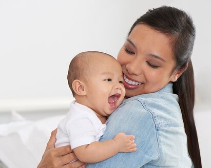 Eine Mutter hält ihr glückliches Baby und lächelt.