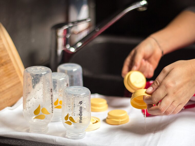A mother washes Medela breast milk bottles and lays them on a towel to dry.