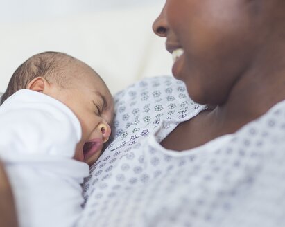 Una madre sonriente sentada en un hospital con su bebé recién nacido en el pecho.