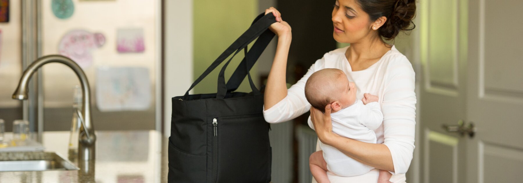 A mom getting ready to leave the house while holding her baby on in the kitchen.