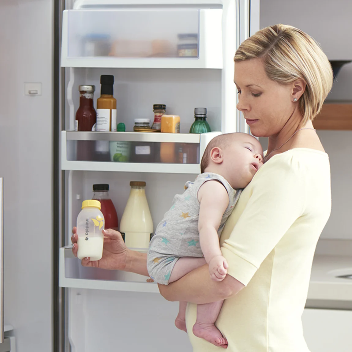 Une maman tient son bébé dans la cuisine pendant qu'elle prépare du lait exprimé réfrigéré pour une tétée.