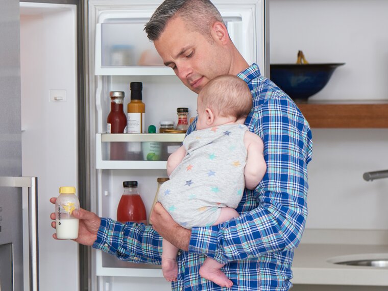 Un père tient son bébé dans la cuisine pendant qu'il sort un biberon du réfrigérateur pour le réchauffer.