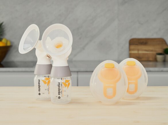 Um conjunto de Copos Colectores Mãos-livres Medela com um kit de extração dupla PersonalFit Flex™ clássico da Medela, tubos não mostrados, pousados num balcão.