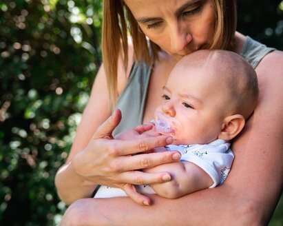 A mother comforts her baby as they sit outside.