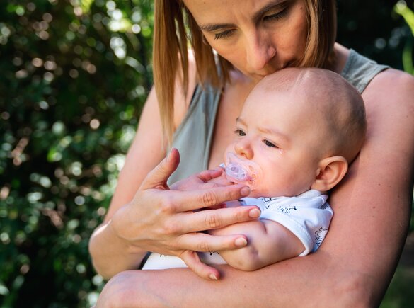 A mother comforts her baby as they sit outside.