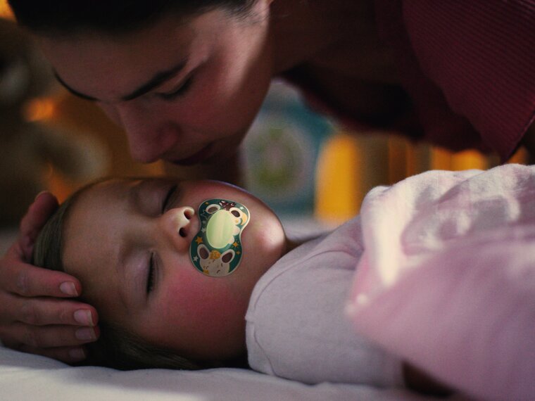 A sick child uses a Medela NIGHT dummy while lying in bed with his mom.