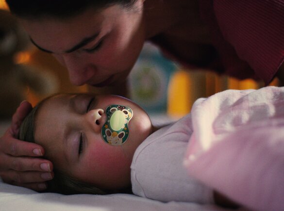 A sick child uses a Medela NIGHT dummy while lying in bed with his mom.