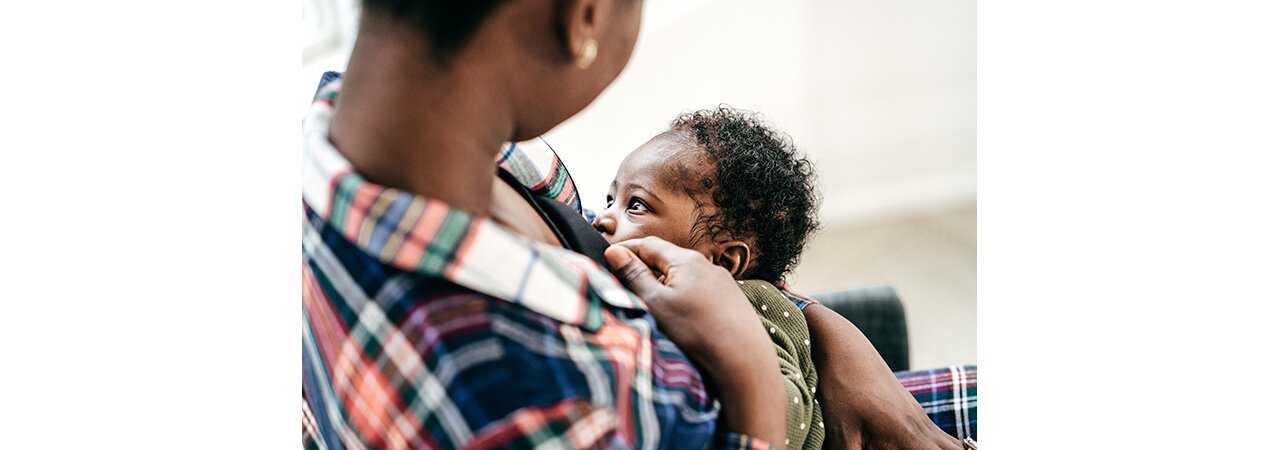 A mother breastfeeding her baby while it faces her.