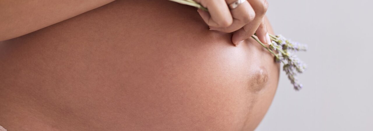 Eine schwangere Mutter steht und hält Lavendel auf ihren Babybauch. 