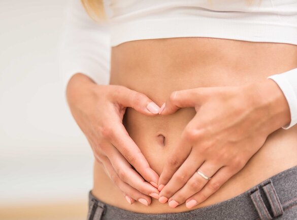 Eine Frau macht mit ihren Händen vor ihrem Bauch die Form eines Herzens.