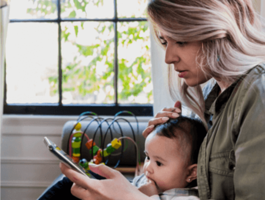 Mom looking at her phone with baby sitting on her lap.