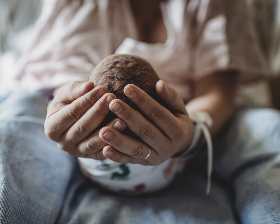 A mother cradles her newborn baby's head in her hands while in the hospital.
