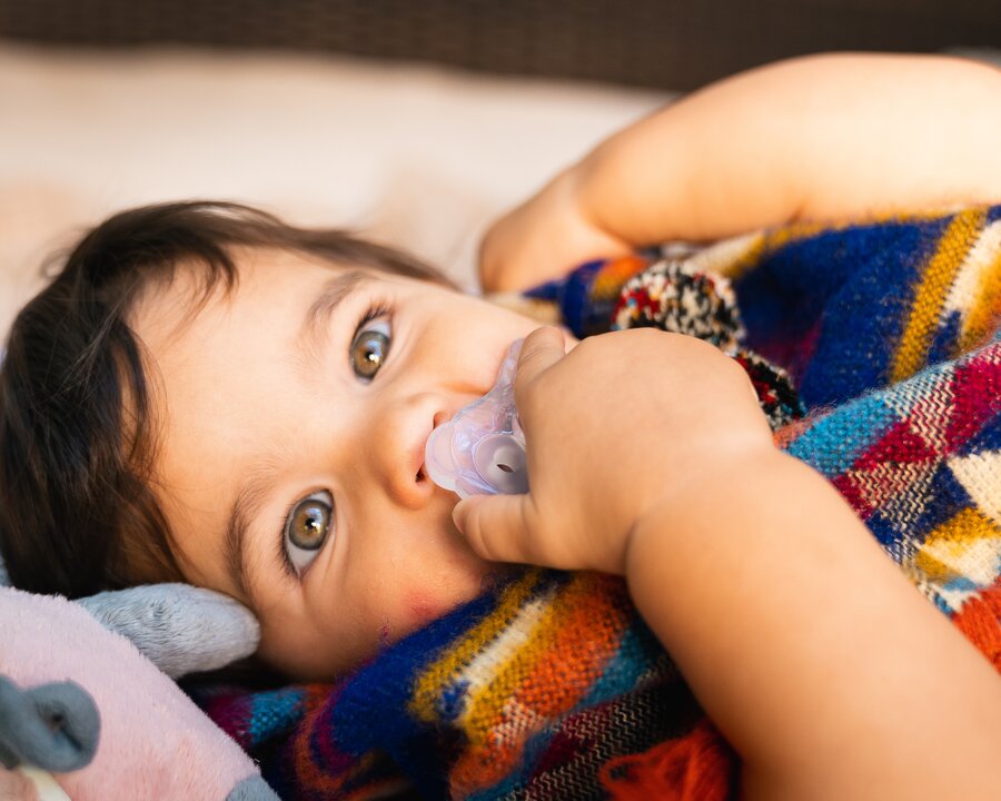 A child lying down with a blanket and its Medela SOFT SILICONE dummy.