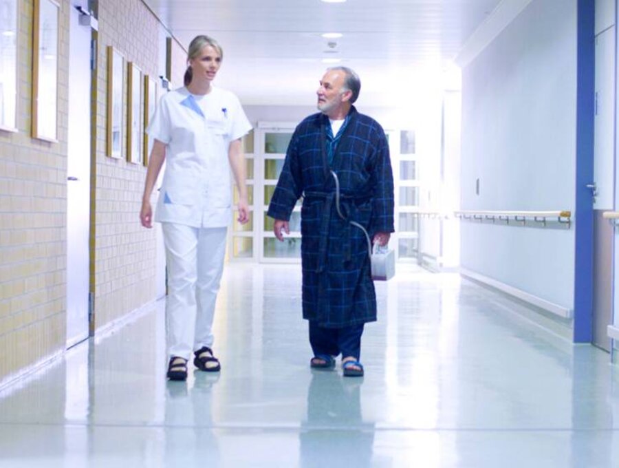 A doctor and a patient walk down a hospital corridor.