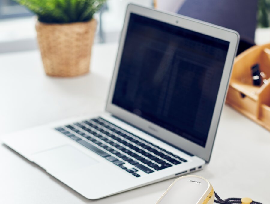 Medela Freestyle Flex sitting next to a laptop computer on a desk.